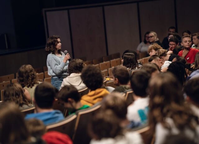 jeune fille parle au micro devant une salle d'&eacute;tudiants en salle de cin&eacute;ma